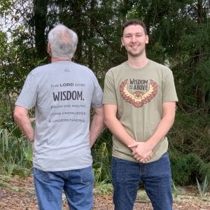 Two male models showing both colors — medium gray and olive green — of Livin' Light's Wisdom Comes From Above T-shirt. They are also modeling the front and back. Proverbs 2:6