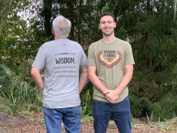 Two male models showing both colors — medium gray and olive green — of Livin' Light's Wisdom Comes From Above T-shirt. They are also modeling the front and back. Proverbs 2:6