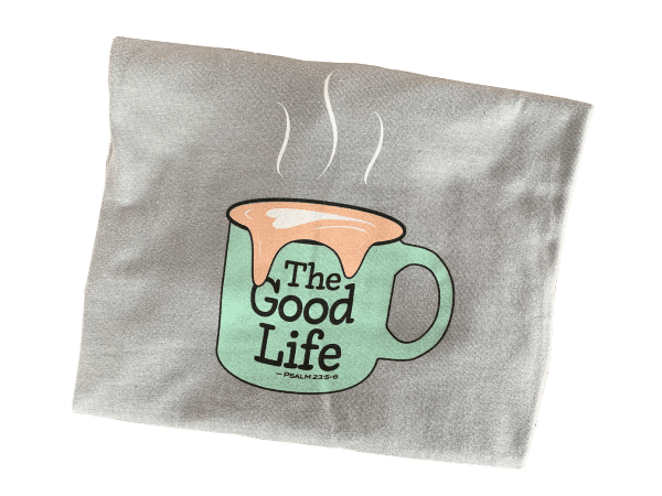 Close up of Livin' Light's The Good Life coffee mug shirt with overflowing froth heart. The extra-large light green mug pops out from the gray shirt. The design illustrates the fulfillment God's abundant love for us.