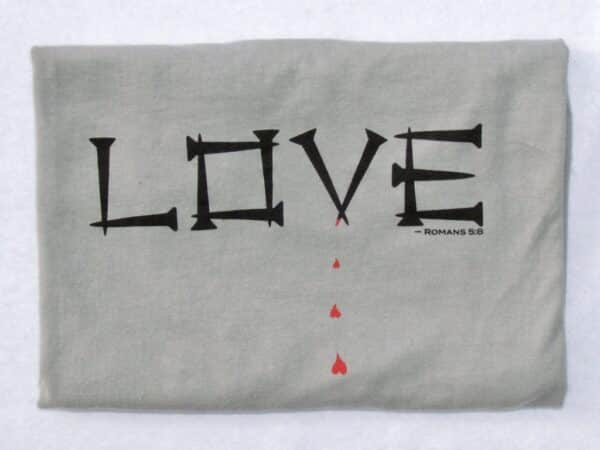 LOVE front: This Livin' Light shirt spells out the word Love in nails. From one nail, blood drips forming into hearts. This bold design on a gray, short-sleeved shirt illustrates Romans 5:8 Jesus loves us so much that He died on the cross to forgive our sins so that we can become clean and have the opportunity to be considered holy again and be saved.
